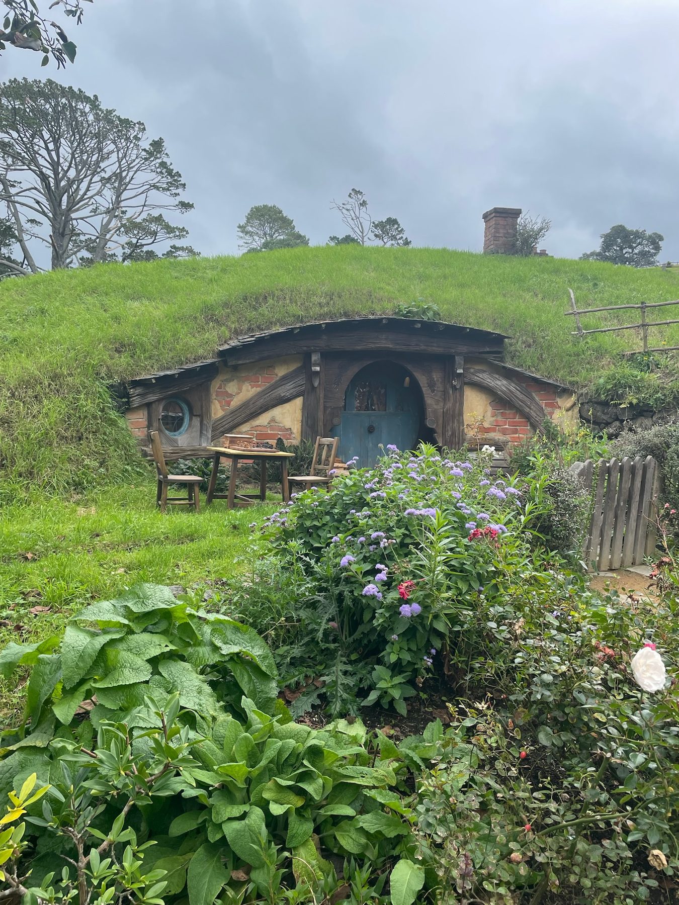 A hobbit hole with a blue door and a flowering garden at Hobbiton